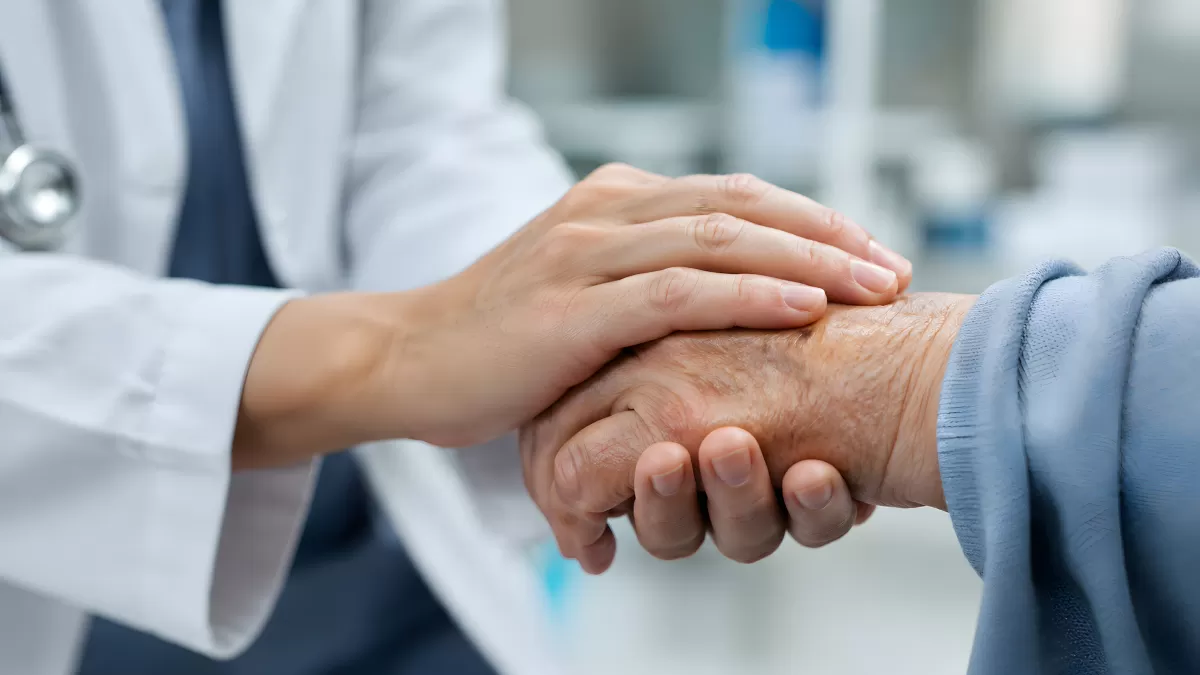 Arzt hält fürsorglich Hand eines älteren Patienten