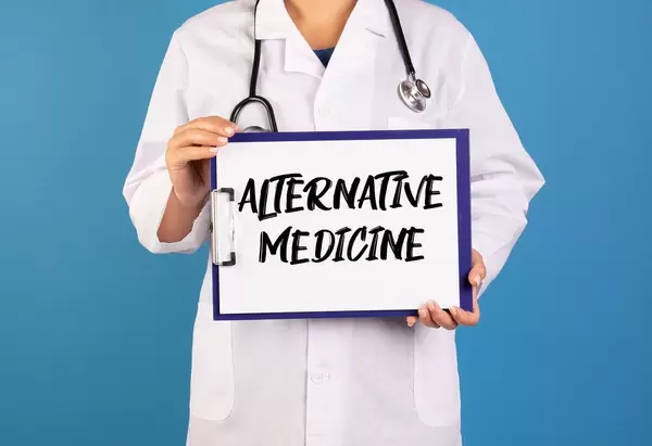 Arzt hält ein Schild mit der Schrift 'Alternative Medicine' im blauen Hintergrund