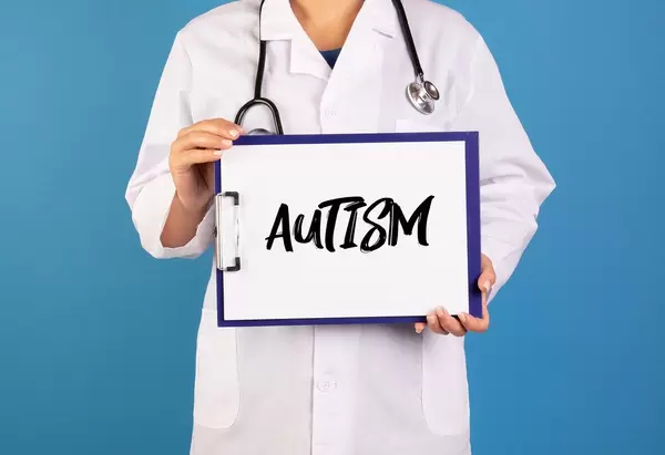 Arzt hält ein Schild mit der Schrift 'Autism' im blauen Hintergrund