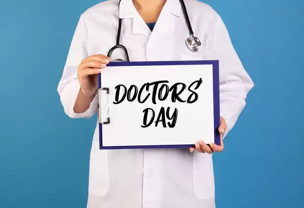 Arzt hält ein Schild mit der Schrift 'Doctor's Day' im blauen Hintergrund