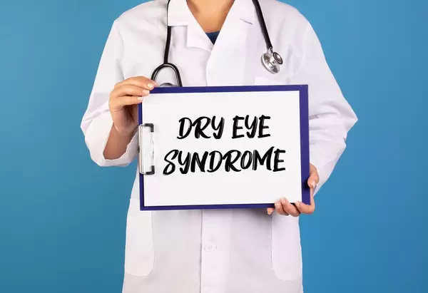 Arzt hält ein Schild mit der Schrift 'Dry Eye Syndrome' im blauen Hintergrund