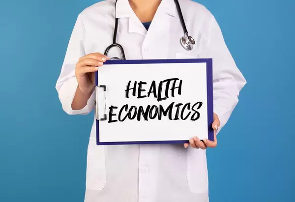 Arzt hält ein Schild mit der Schrift 'Health economics' im blauen Hintergrund