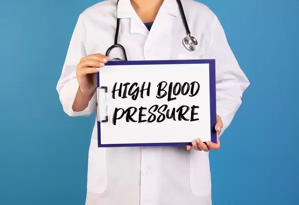 Arzt hält ein Schild mit der Schrift 'High Blood Pressure' im blauen Hintergrund