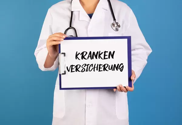 Arzt hält ein Schild mit der Schrift 'Krankenversicherung' im blauen Hintergrund