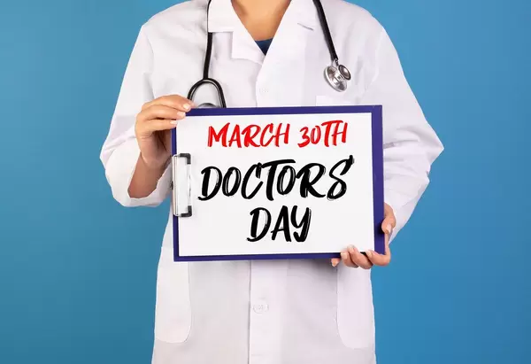 Arzt hält ein Schild mit der Schrift 'March 30th - Doctor's Day' im blauen Hintergrund