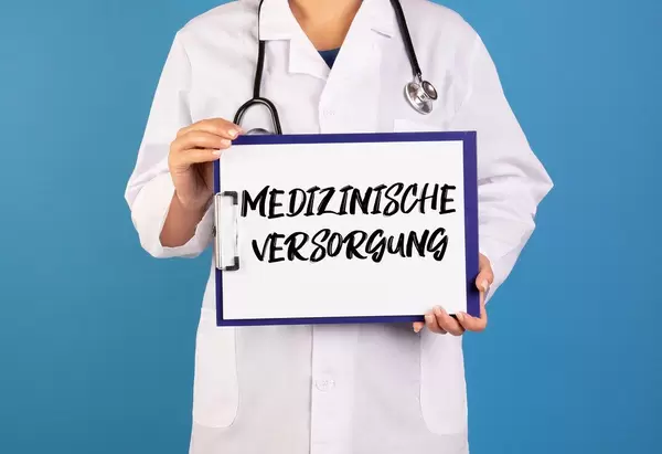 Arzt hält ein Schild mit der Schrift 'Medizinische Versorgung' im blauen Hintergrund