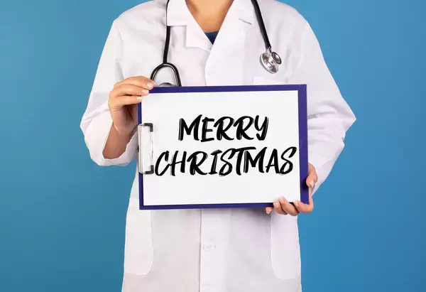 Arzt hält ein Schild mit der Schrift 'Merry Christmas' im blauen Hintergrund