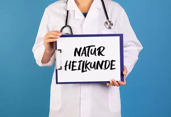 Arzt hält ein Schild mit der Schrift 'Naturheilkunde' im blauen Hintergrund
