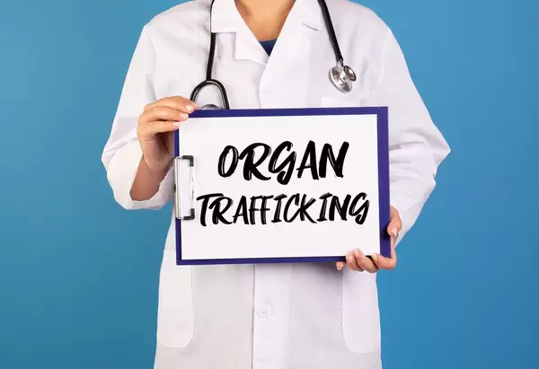 Arzt hält ein Schild mit der Schrift 'Organ Trafficking' im blauen Hintergrund