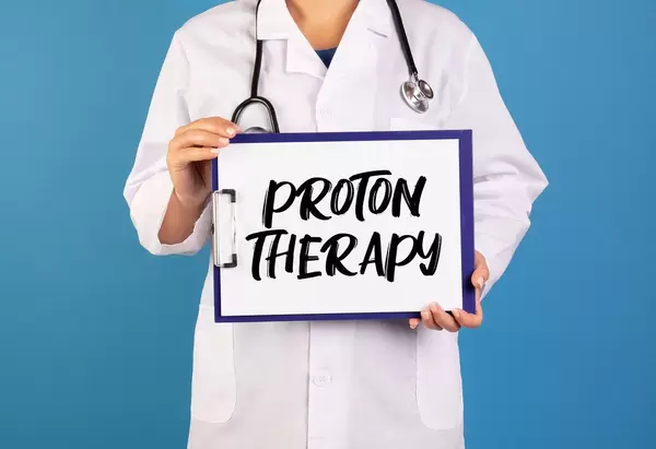 Arzt hält ein Schild mit der Schrift 'Proton Therapy' im blauen Hintergrund