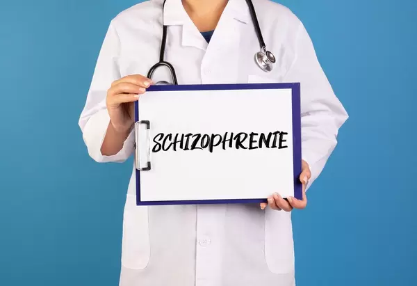 Arzt hält ein Schild mit der Schrift 'Schizophrenie' im blauen Hintergrund