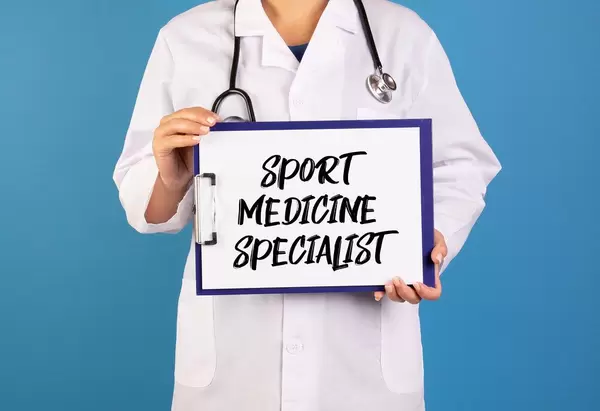 Arzt hält ein Schild mit der Schrift 'Sport Medicine Specialist' im blauen Hintergrund
