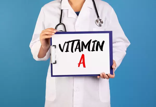Arzt hält ein Schild mit der Schrift 'Vitamin A' im blauen Hintergrund