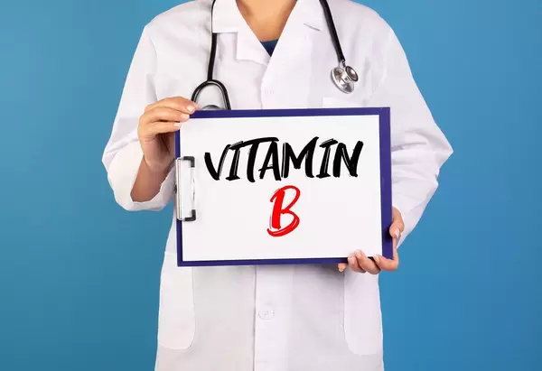 Arzt hält ein Schild mit der Schrift 'Vitamin B' im blauen Hintergrund