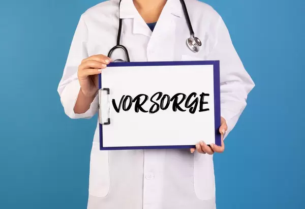Arzt hält ein Schild mit der Schrift 'Vorsorge' im blauen Hintergrund