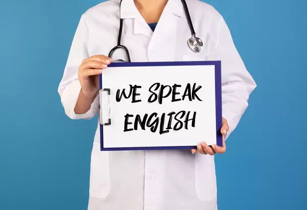 Arzt hält ein Schild mit der Schrift 'We speak English' im blauen Hintergrund