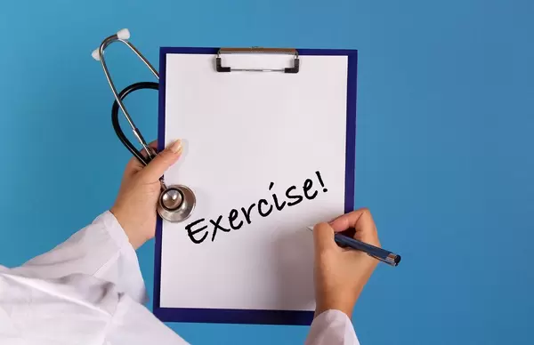 Arzt mit einem Stethoskop in der Hand hält ein Schild mit der Schrift 'Exercise!'