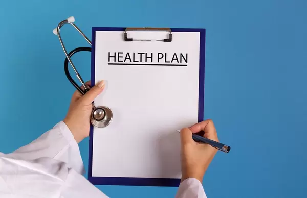 Arzt mit einem Stethoskop in der Hand hält ein Schild mit der Schrift 'Health Plan'