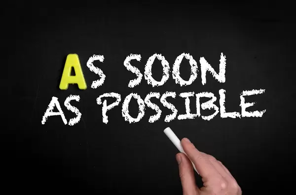 ASAP: Hand schreibt  "As soon as possible" - So bald wie möglich - mit Kreide auf eine schwarze Tafel