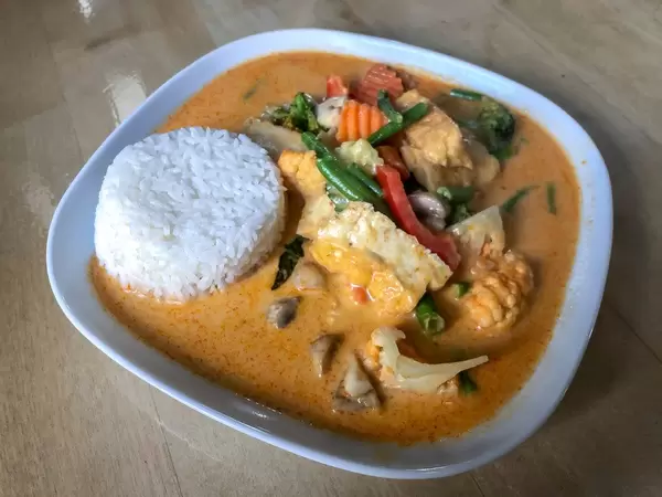 Asian Lunch with tofu thai and spicy curry sauce, coconut milk, rice, cream and fresh vegetables on a wooden table