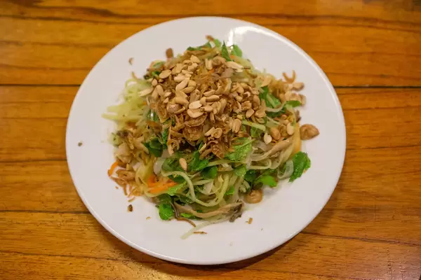Asiatischer Papaya Salat mit Karotten, Minze, Röstzwiebeln, Gerösteten Erdnüssen und Fischsauce auf einem Teller von oben auf einem Holztisch fotografiert