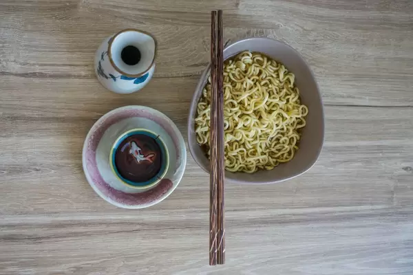 Asiatisches Frühstück aus Schüssel mit Nudeln, Essstäbchen und Tee auf Holztisch von oben fotografiert