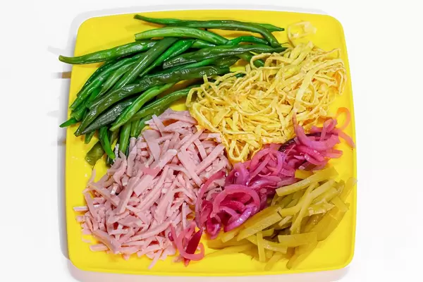 Asparagus beans, sliced ham and scrambled eggs, pickled purple onion and cucumbers on a yellow plate. Top view (Flip 2019)