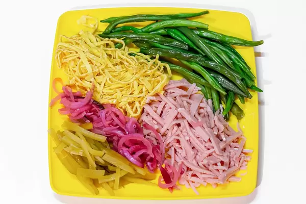 Asparagus beans, sliced ham and scrambled eggs, pickled purple onion and cucumbers on a yellow plate. Top view