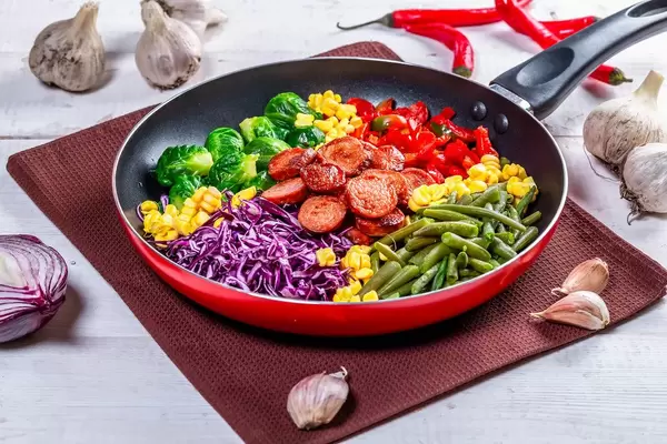 Asparagus, Brussels sprouts, corn, peppers and sausages in a frying pan (Flip 2019)