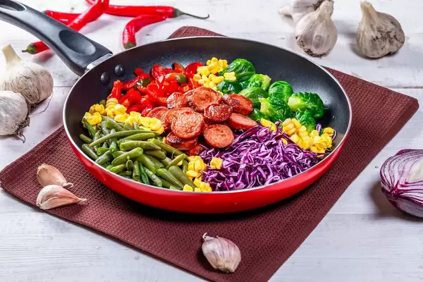 Asparagus, Brussels sprouts, corn, peppers and sausages in a frying pan