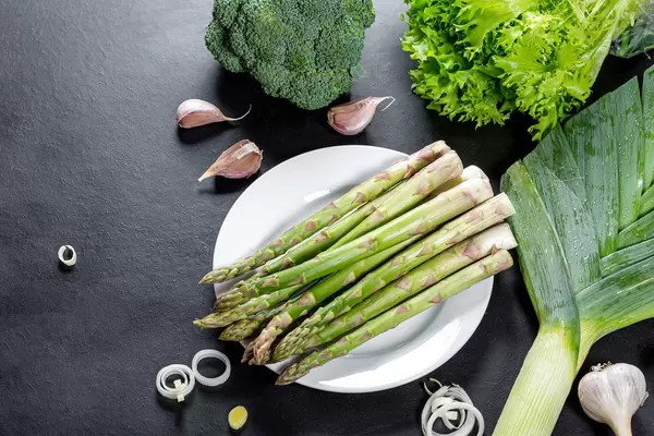 Asparagus, lettuce, broccoli, leeks and garlic on black background. Top view