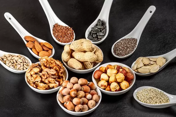 Assortment of nuts and seeds in white bowls and spoons on a black background, close- up (Flip 2020)