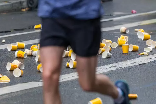 Athlet läuft an der Verpflegungsstation vorbei mit Becher auf dem Boden