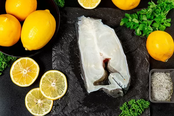 Atlantic wolffish steak on dark background with lemons slices