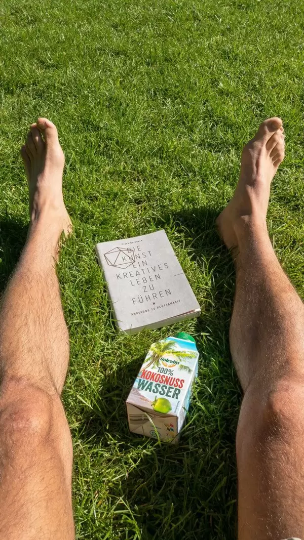Auf dem Rasen liegen mit Buch und Kokosnusswasser