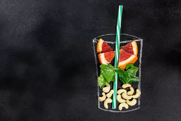 Auf schwarzem Hintergrund gekreidetes Glas mit frischer Grapefruit und Cashews