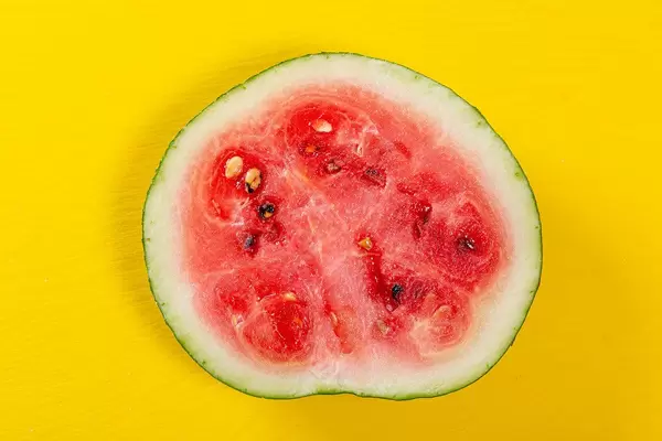 Aufgeschnittene, halbierte Wassermelone mit Kernen, auf einem gelben Tisch