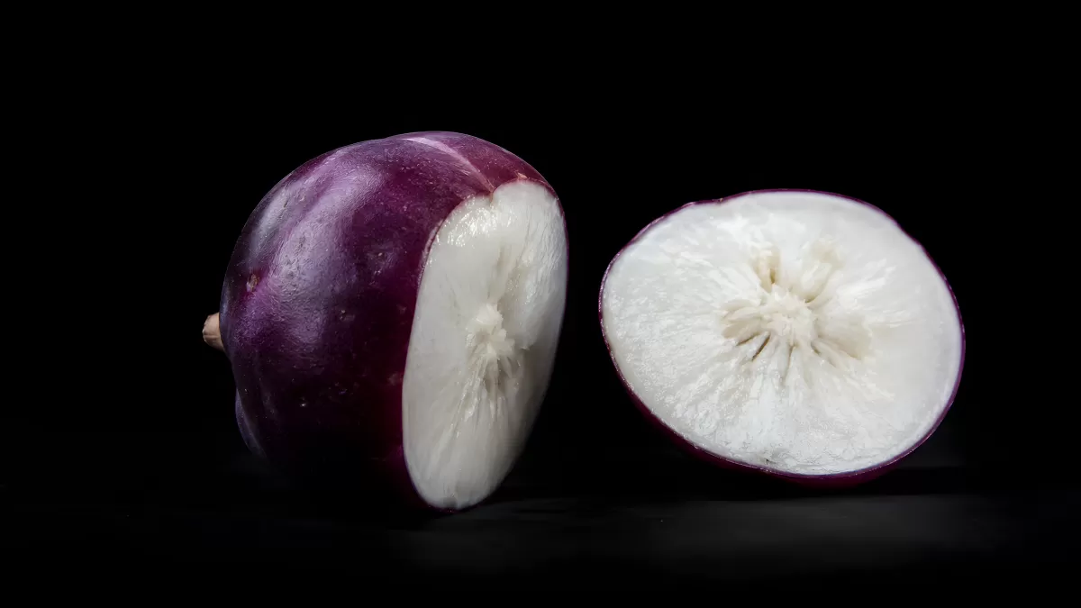 Aufgeschnittene Sternapfel-Frucht vor schwarzem Hintergrund