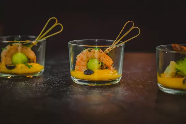 Aufgespießte Schrimps in Mango-Soße garniert mit schwarzen und grünen Oliven - Nahaufnahme in Seitenansicht