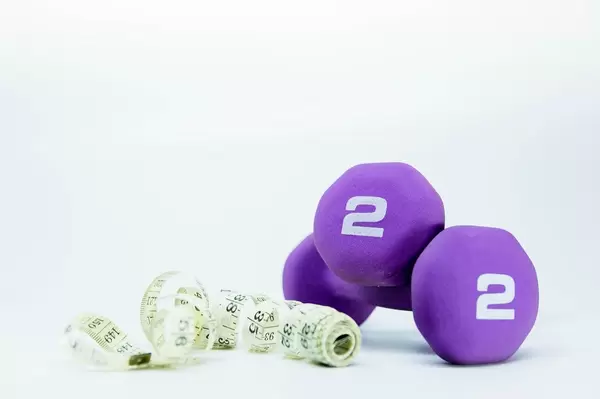 Aufgewickeltes Maßband und zwei Pfund schwere Fitnessgewichte vor weißem Hintergrund