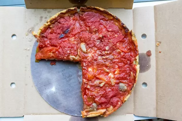 Aufnahme von oben: drei Viertel einer typischen Chicago Deep Dish Pizza von Pizzeria Uno mit Käse und Tomaten und mit hohem Rand