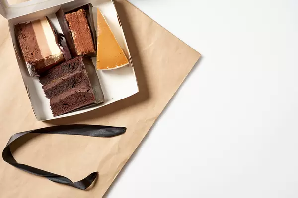 Aufnahme von oben: eine offene Box mit vier verschiedenen Tortenstücken auf einer Papiertüte