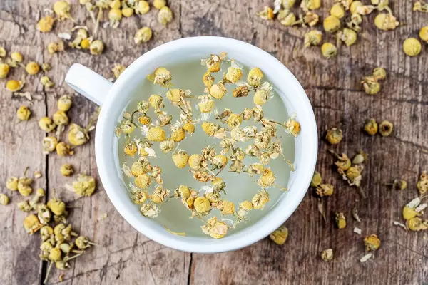Aufnahme von oben: eine Tasse Kamillentee auf einem alten hölzernen Hintergrund