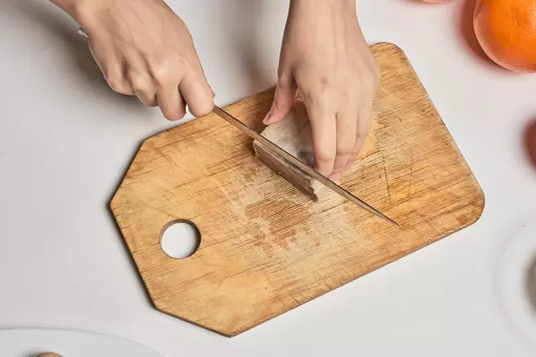 Aufnahme von oben: Hände mit Messer schneiden zubereitetes Rinderzungefleisch auf einem Holzbrett