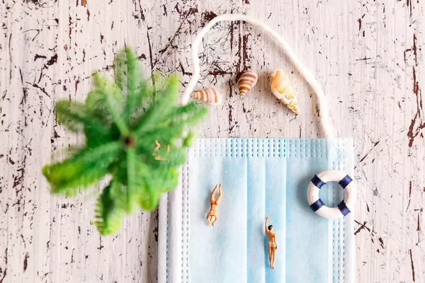 Aufnahme von oben: Miniaturfiguren schwimmen auf OP-Maske. Am Strand in Zeiten von Corona