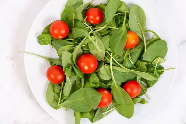 Aufnahme von oben von Teller mit ganzen Cherry-Tomaten auf Babyspinat