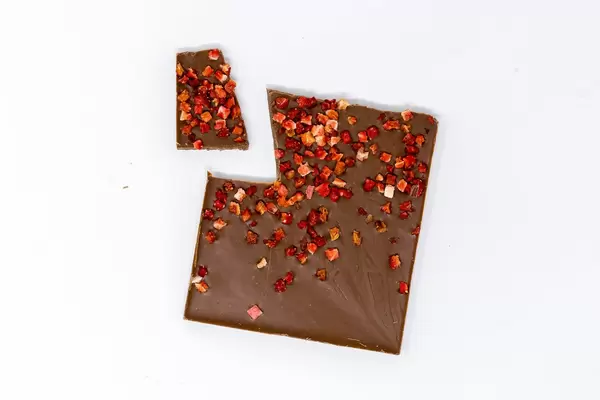 Aufsicht auf eine Bio Protein Schokolade mit Erdbeerstückchen mit einer abgebrochenen Ecke auf weißem Hintergrund