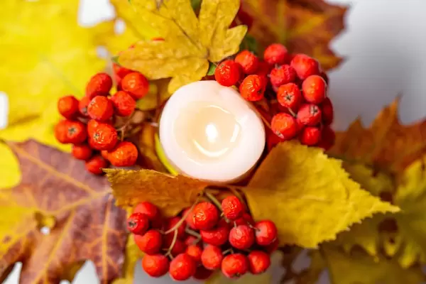 Aufsicht auf eine leuchtende Kerze mit roten Beeren und gelben Blättern als Herbstdekoration