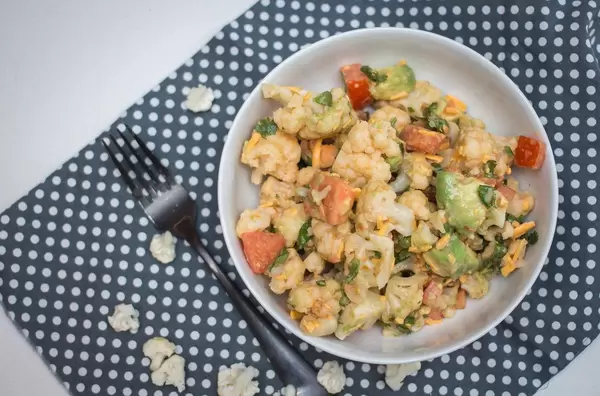 Aufsicht - Blumenkohl Salat, mit Avocado, Möhren und Tomaten in einer Schale auf gepunktetem Platzdeckchen