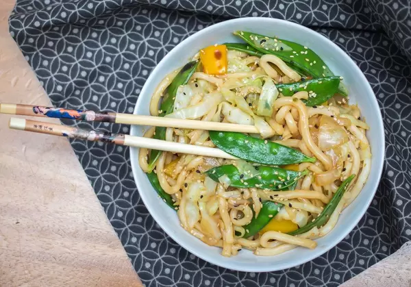 Aufsicht - Chow Mein Nudeln mit grünen Bohnen und Sesam in einer Schale mit Essstäbchen